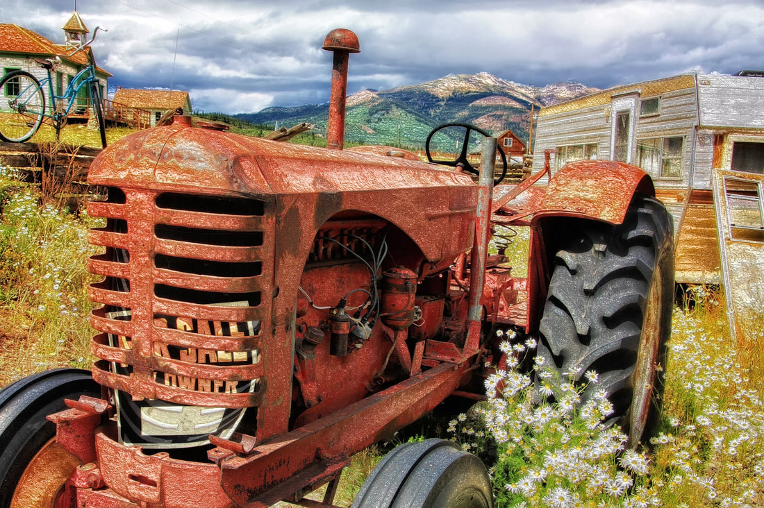 Old tractor with a For Sale sign in the front grill. Trailer and house in the background. 