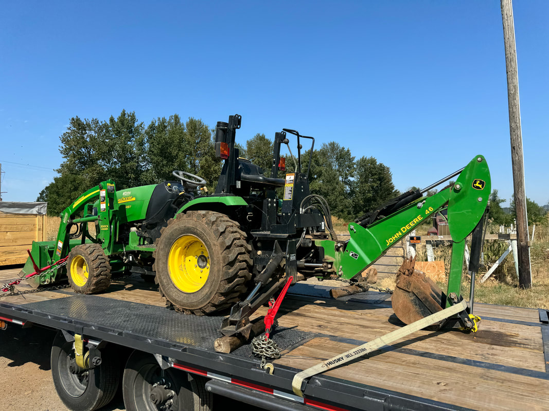 Farm equipment transport shown by John Deere tractor with loader and backhoe loaded on gooseneck trailer. Logi Transports