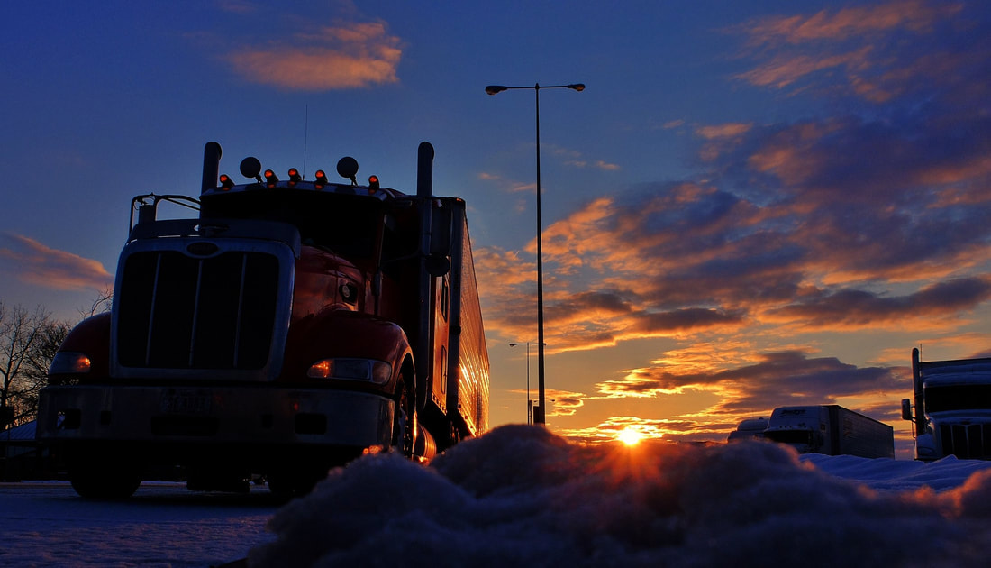 Semi truck with setting sun and snow on the ground.