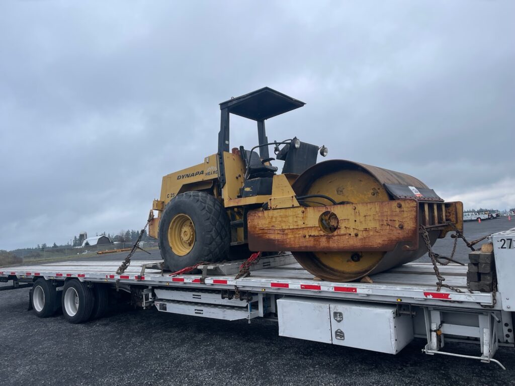 Roller going to port delivery loaded on step deck trailer with ramps.